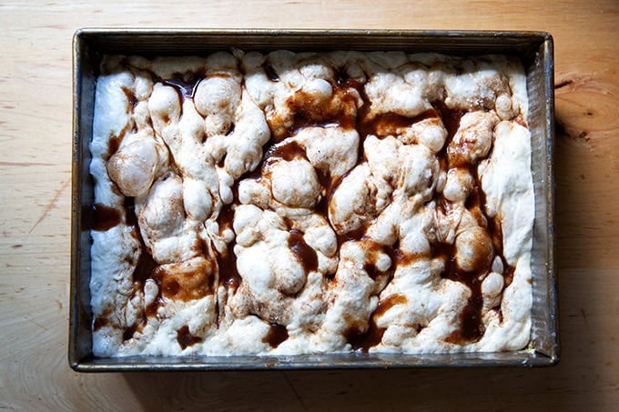 A dimpled cinnamon-sugar focaccia dough in a 9x13-inch pan, ready to be baked.