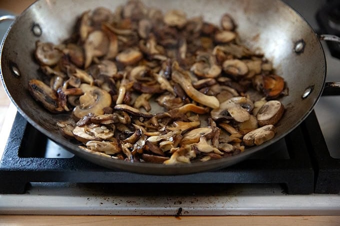 A large pan on the stovetop filled with browned mushrooms for turkey tetrazzini.
