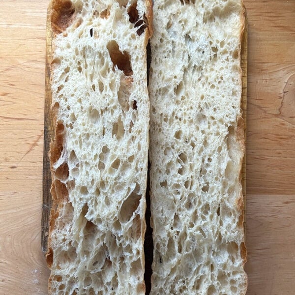 Giant sandwich roll dough, halved on a cutting board.