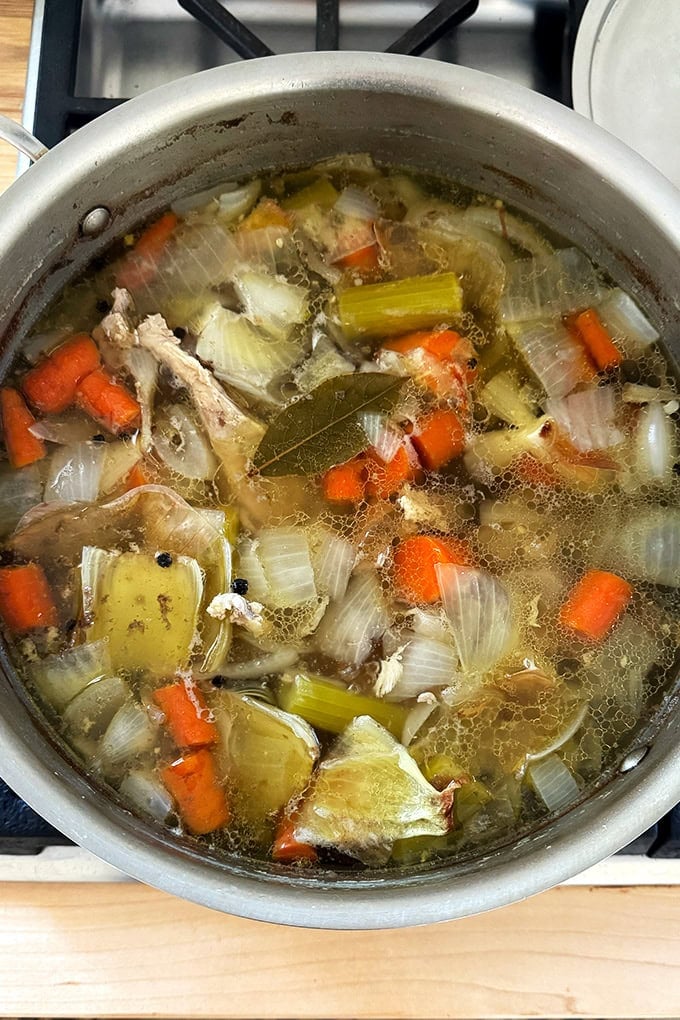 A pot of water, vegetables and chicken bones simmering on the stovetop.