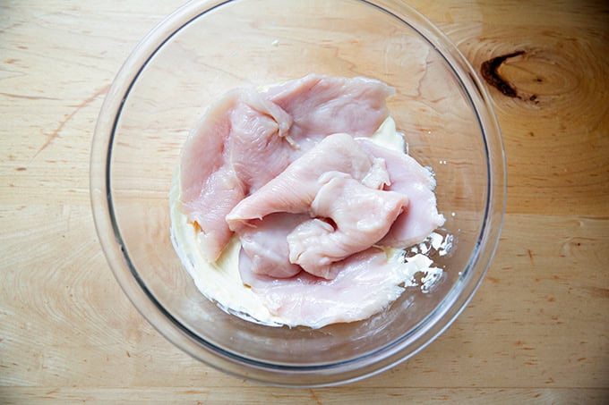 Chicken cutlet in a bowl filled with a mayonnaise-mustard mixture.