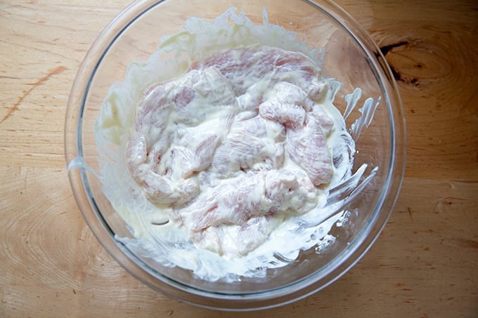 A large bowl filled with chicken cutlets coated in a mayonnaise mustard mixture.