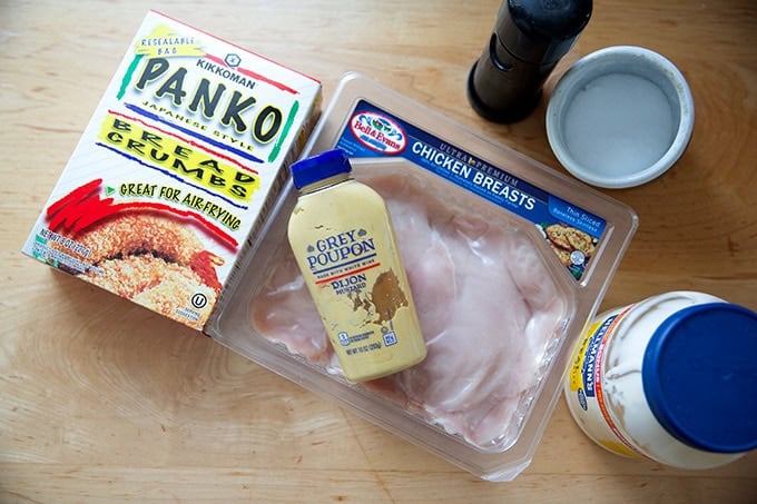 The ingredients to make chicken cutlets on a countertop: panko bread crumbs, thinly sliced chicken breasts, mustard, mayonnaise, salt, and pepper.