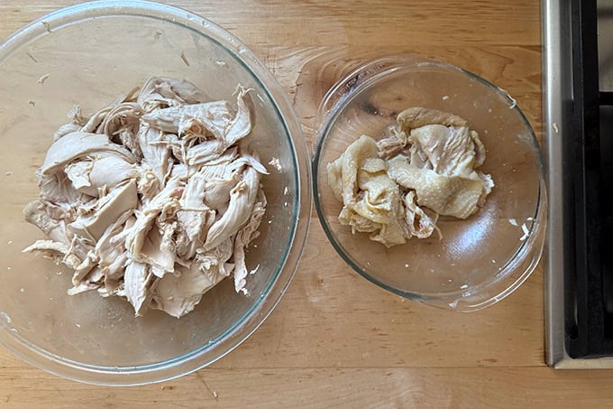 A large bowl filled with pulled chicken aside a small bowl filled with chicken skin.