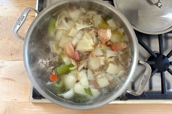 A large pot filled with water, chicken pieces and vegetables simmering to make stock.