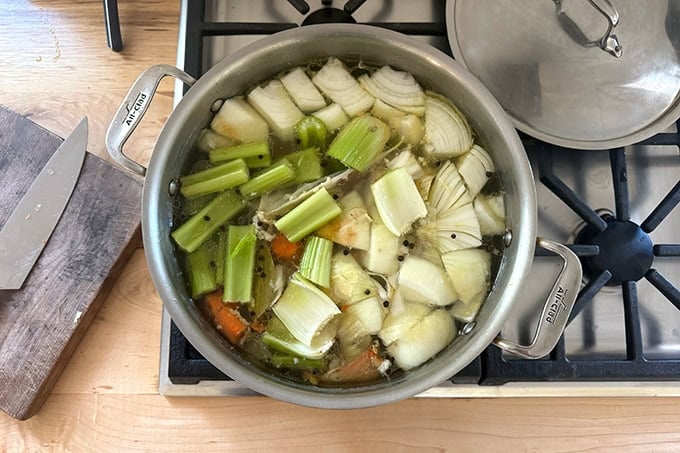A large pot filled with water, chicken pieces and vegetables coming to a simmer to make stock.