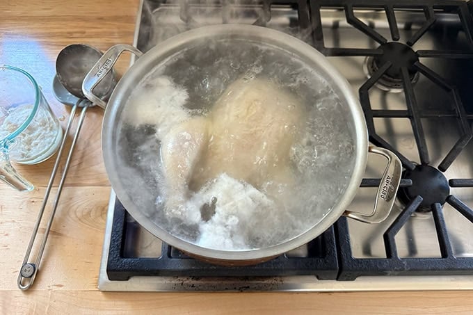 A large pot on the stovetop filled with boiling water and a whole chicken.