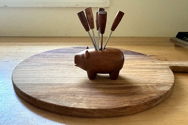 A wooden cheese pick pig atop a wooden cutting board.