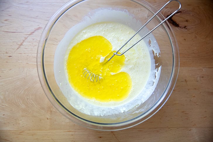 Melted butter added to the wet ingredients to make cornbread in a large bowl.