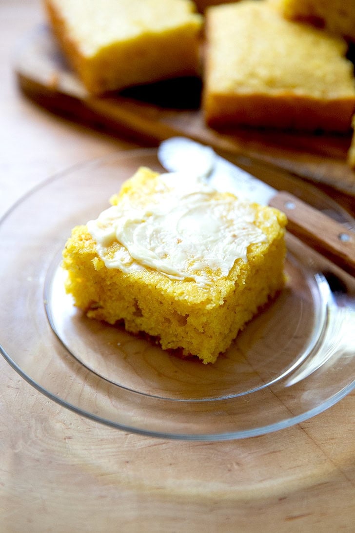 A piece of cornbread, spread with butter, on a small glass plate.