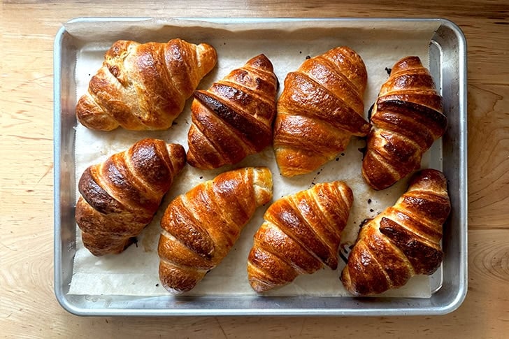Eight croissants, freshly baked, on a sheet pan.