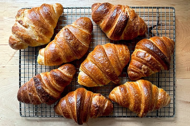 Eight croissants, freshly baked, on a cooling rack.