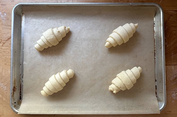 Four unbaked croissants on a sheet pan.