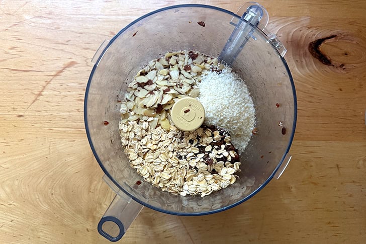Oats, almonds and coconut added to the food processor holding puréed dates.