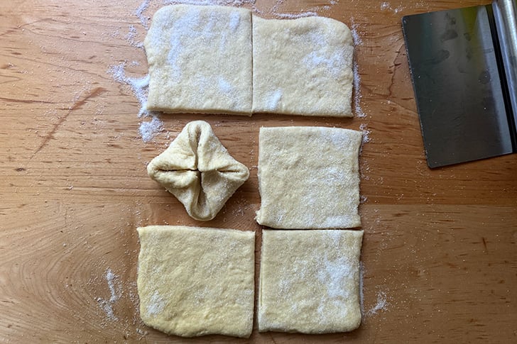 One pinched Kouign-Amann next to 5 squares of dough ready to be pinched.