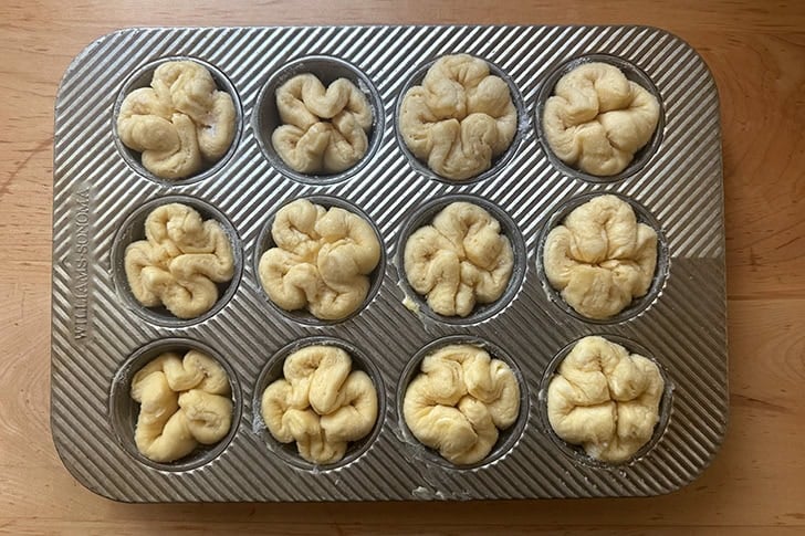 A muffin tin filled with proofed Kouign-Amann, ready to be baked.